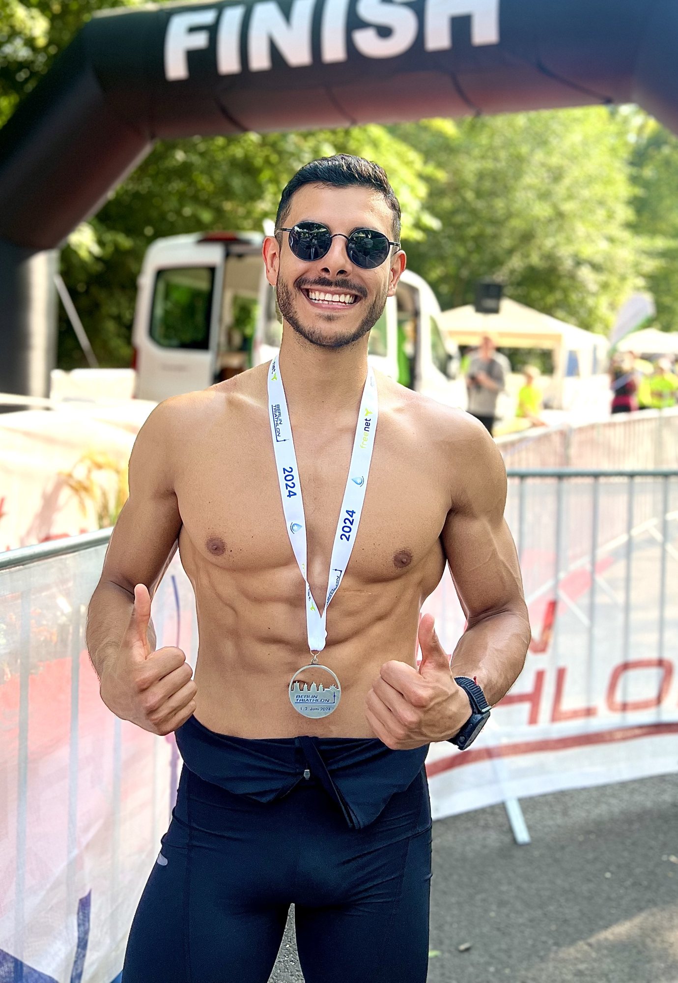 Angelo smiling at a triathlon finish line wearing a 2024 medal